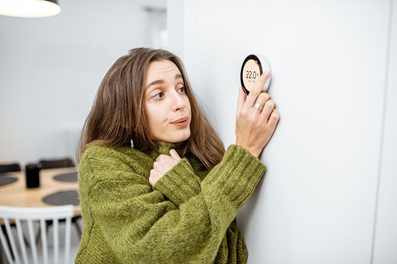 How to Lower Your Winter Heating Bill - Woman Adjusting the Thermostat.