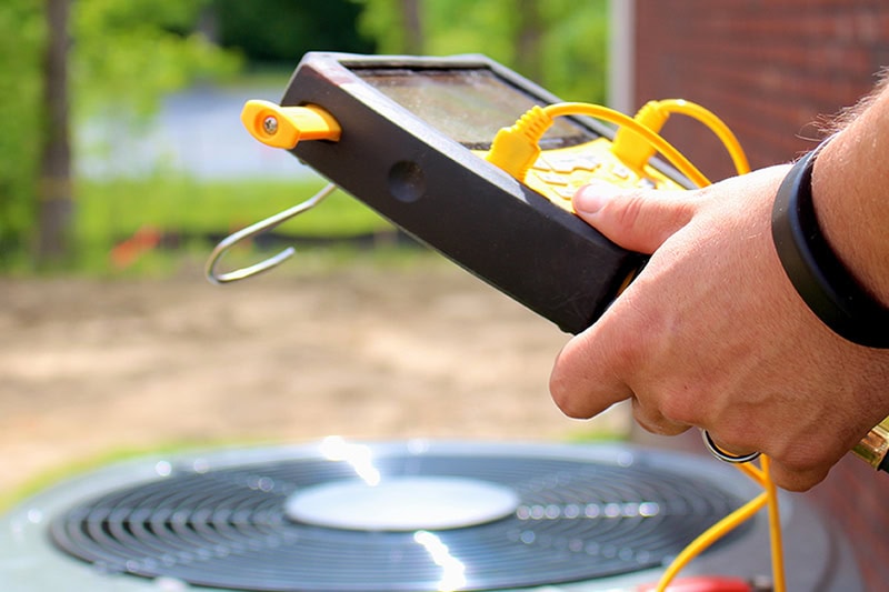 Why Is My AC Short Cycling? A technician using a multimeter on an AC unit.